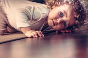 Scared child hiding under the bed in kid room and looking scared
